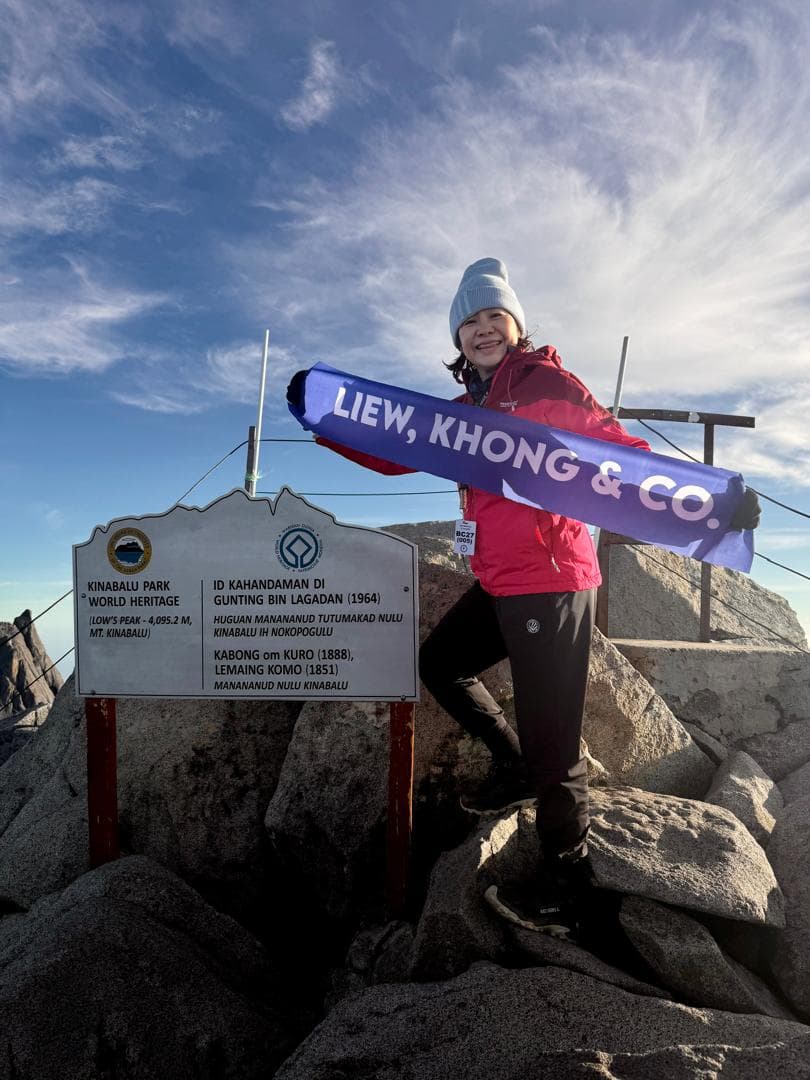 Liew Ngan Fung at Low's Peak holding the Liew, Khong & Co banner beside the Kinabalu Park summit marker.
